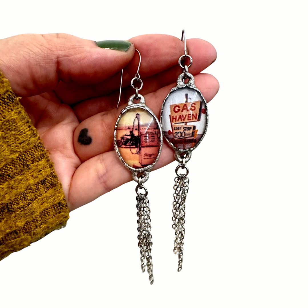 Silver long fringe earrings featuring a mismatched gas station road sign design, inspired by FOXLARK's Road To Nowhere collection.